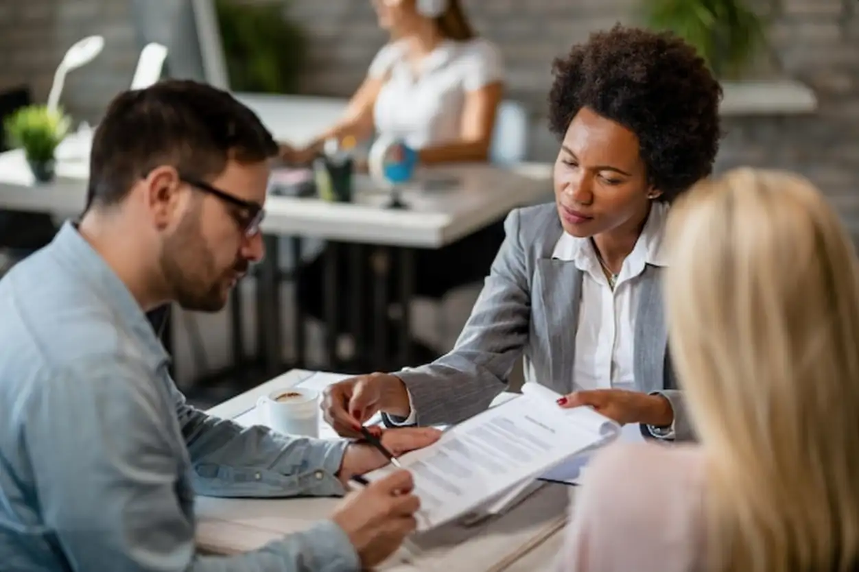 Black female real estate agent showing to a couple where to sign the contract during the meeting in the office