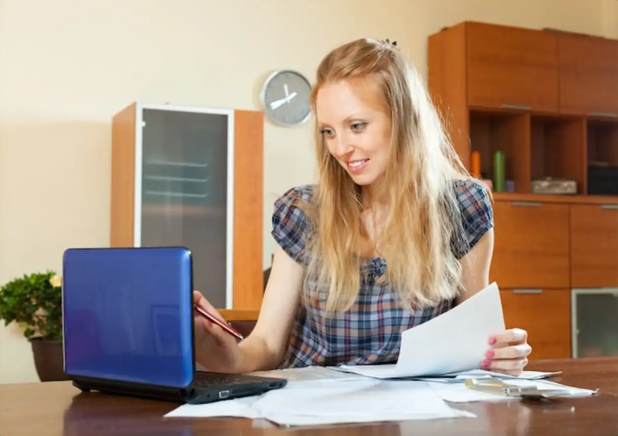 Positive long-haired woman working with documents and laptop