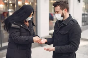 People wearing a protective mask standing on the street while using alcohol gel