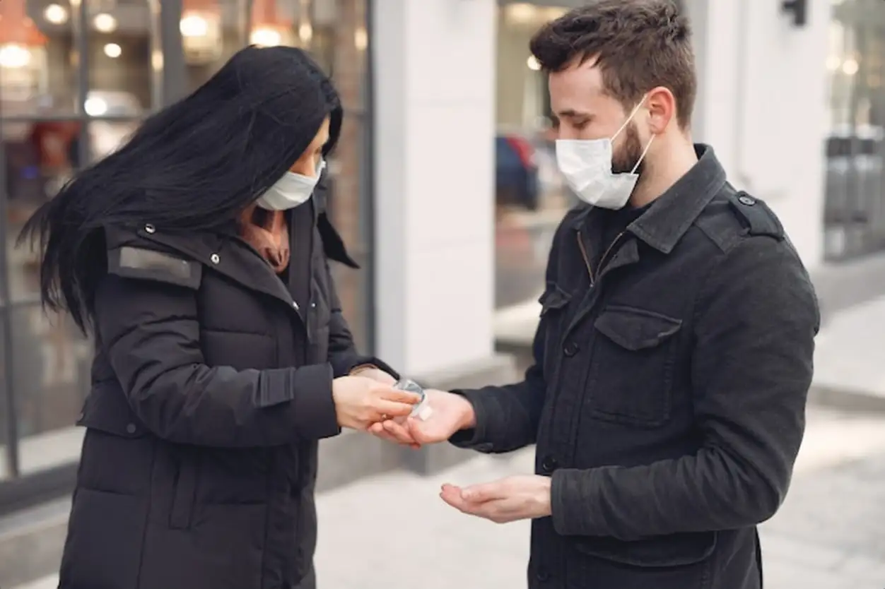 People wearing a protective mask standing on the street while using alcohol gel